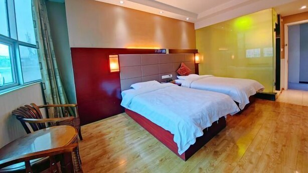 Habitación de hotel con dos camas, piso de madera, pared de acento roja y ventana con cortinas.