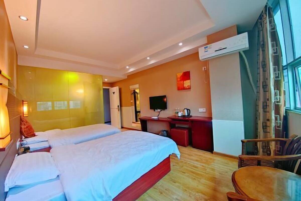 Habitación de hotel con dos camas, un escritorio, una silla y un ventanal grande.