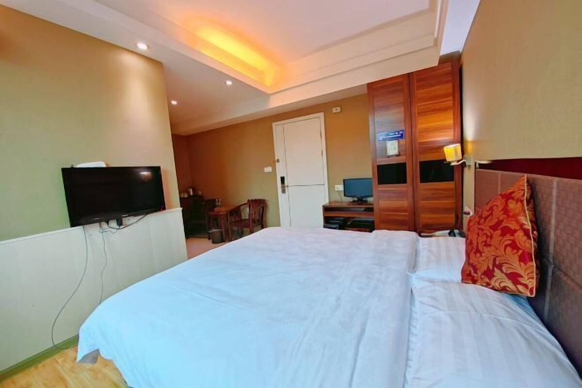 Una habitación de hotel con una cama, televisor, escritorio con ordenador y puerta.