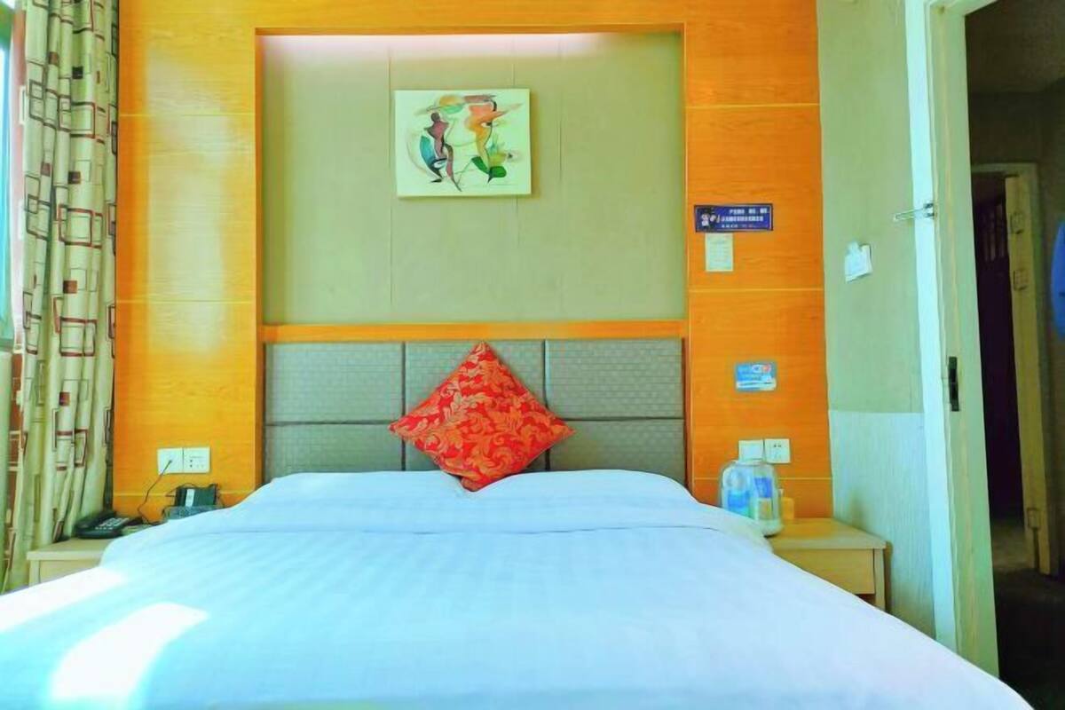 Una habitación de hotel con cama, almohada roja, un cuadro en la pared y un cartel con el número de la habitación.