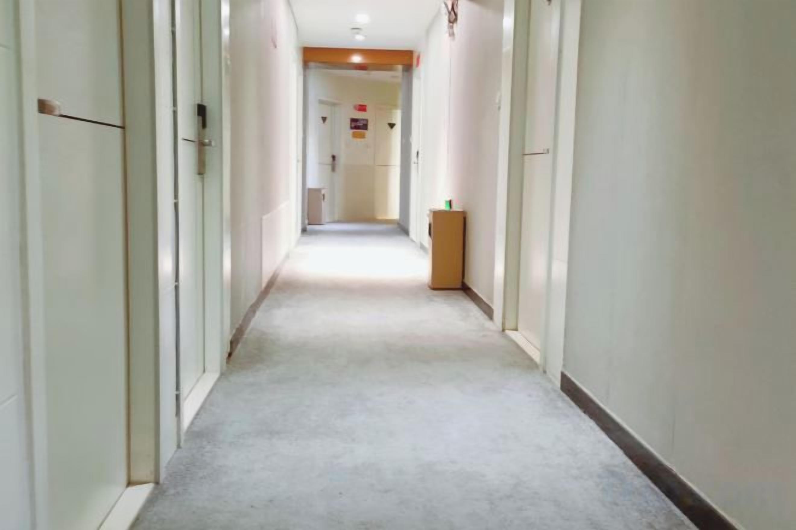 A long, narrow hallway with doors on both sides, leading to a room at the end.