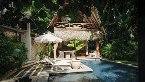 A pool area with a thatched-roof structure, lounge chairs, and a potted plant. - Casa Primos - Luxury Home, Casa Primos - Luxury Home - 2 Min Walk to the Beach (Nosara)