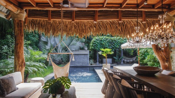 A wooden deck with a hanging chair, a dining table, and a pool. - Casa Primos - Luxury Home, Casa Primos - Luxury Home - 2 Min Walk to the Beach (Nosara)