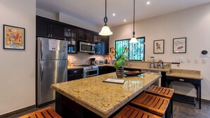 Une cuisine moderne dotée de plans de travail en granit, d’appareils électroménagers en acier inoxydable et de tabourets de bar en bois.