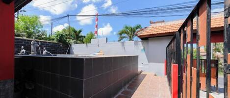 A covered outdoor area with a tiled floor, a black tiled structure, and a red wall.