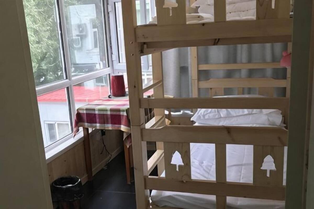 A bunk bed room with a window, a table with a checkered tablecloth, and a chair.