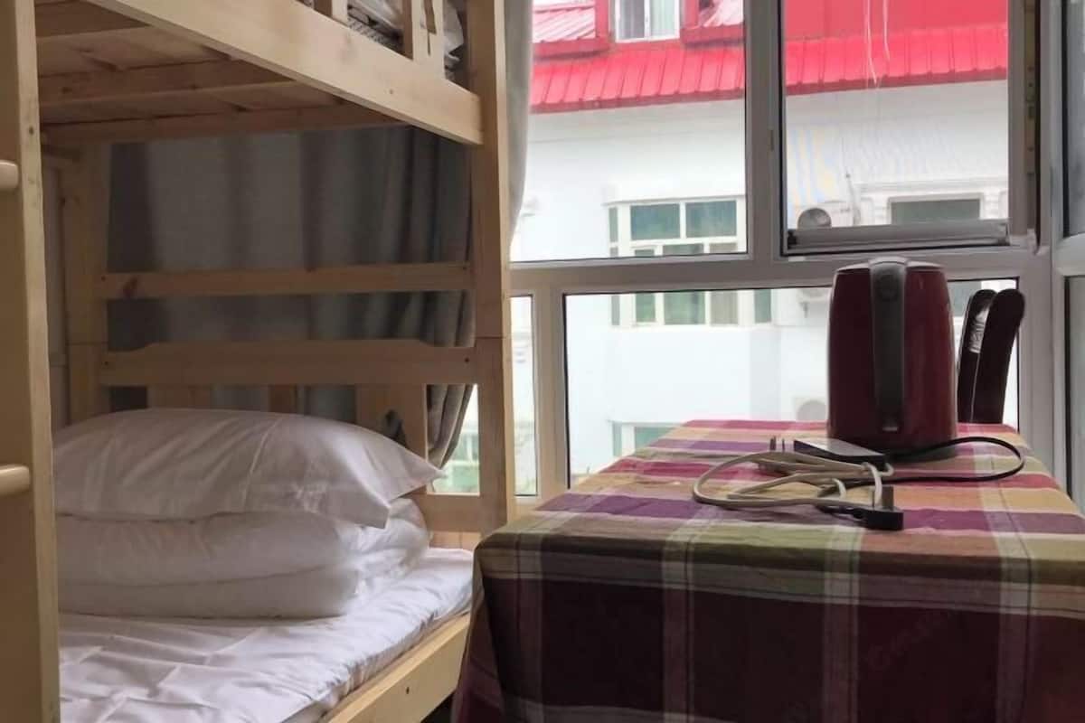 A bunk bed with white bedding, a table with a plaid tablecloth, and a red appliance on the windowsill.