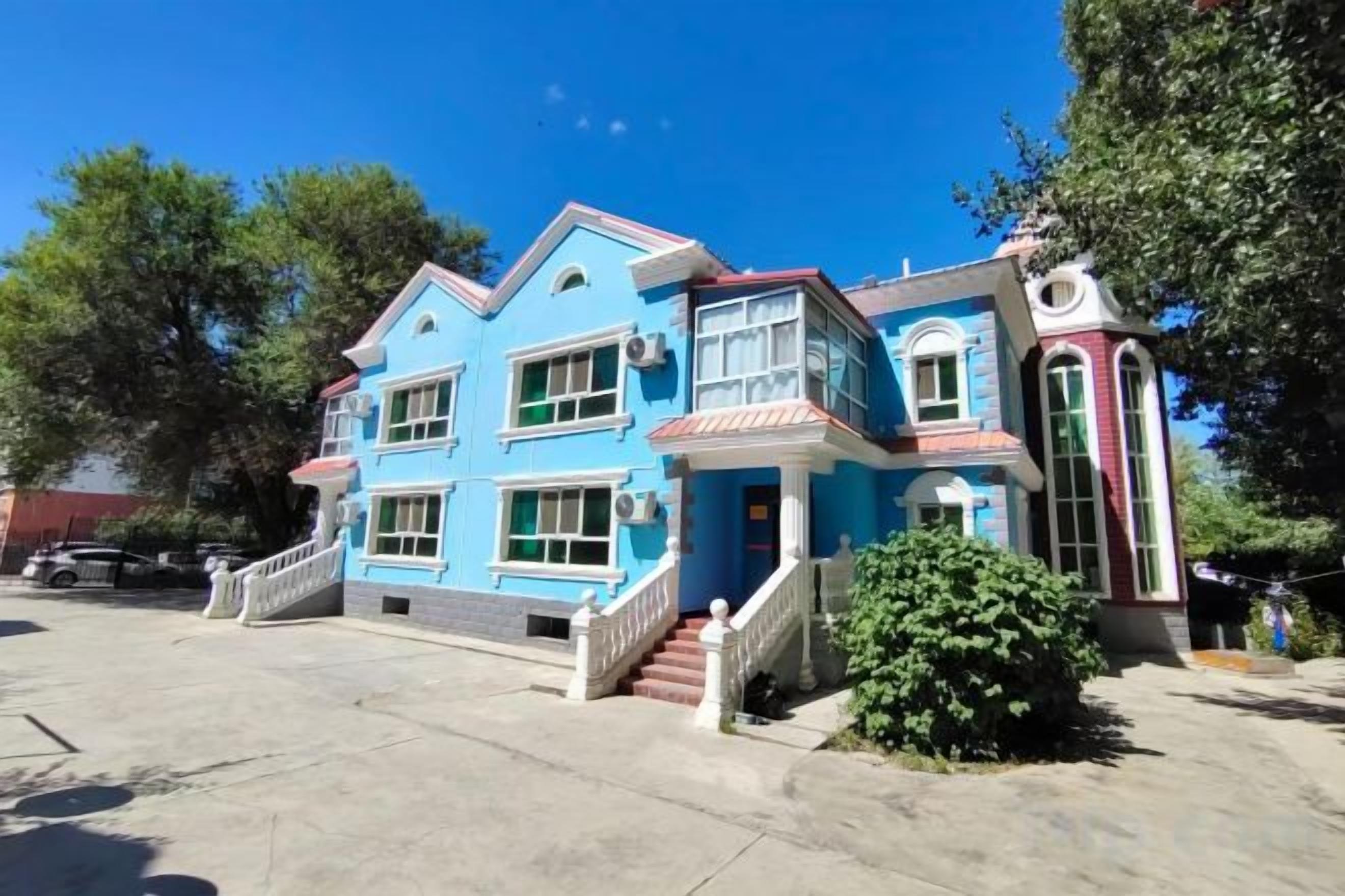 A two-story building with a prominent staircase leading to the entrance, a small porch area, and a clear sky.