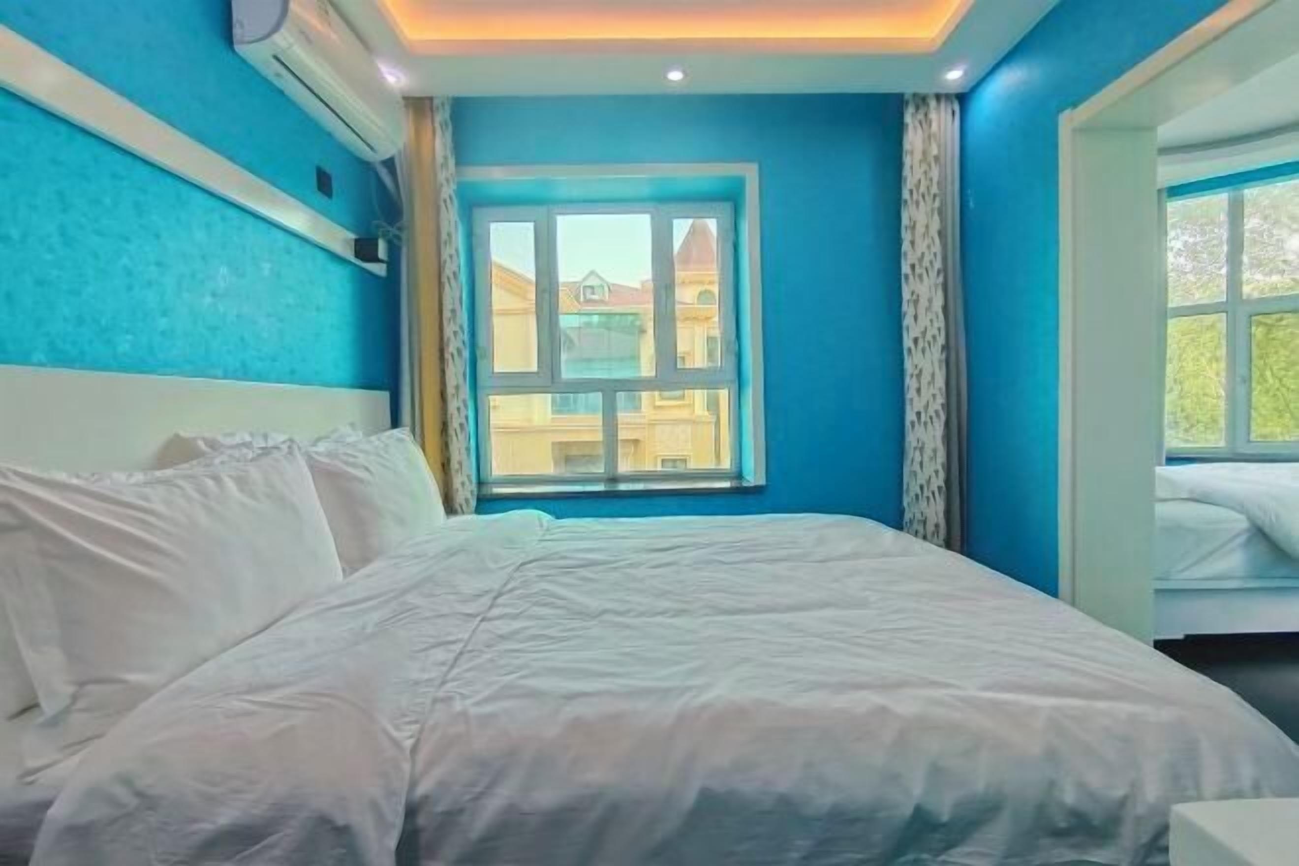 A bedroom with a large bed, a window with a view of buildings, and a ceiling with recessed lighting.