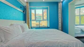 A bedroom with a large bed, a window with a view of buildings, and a ceiling with recessed lighting.