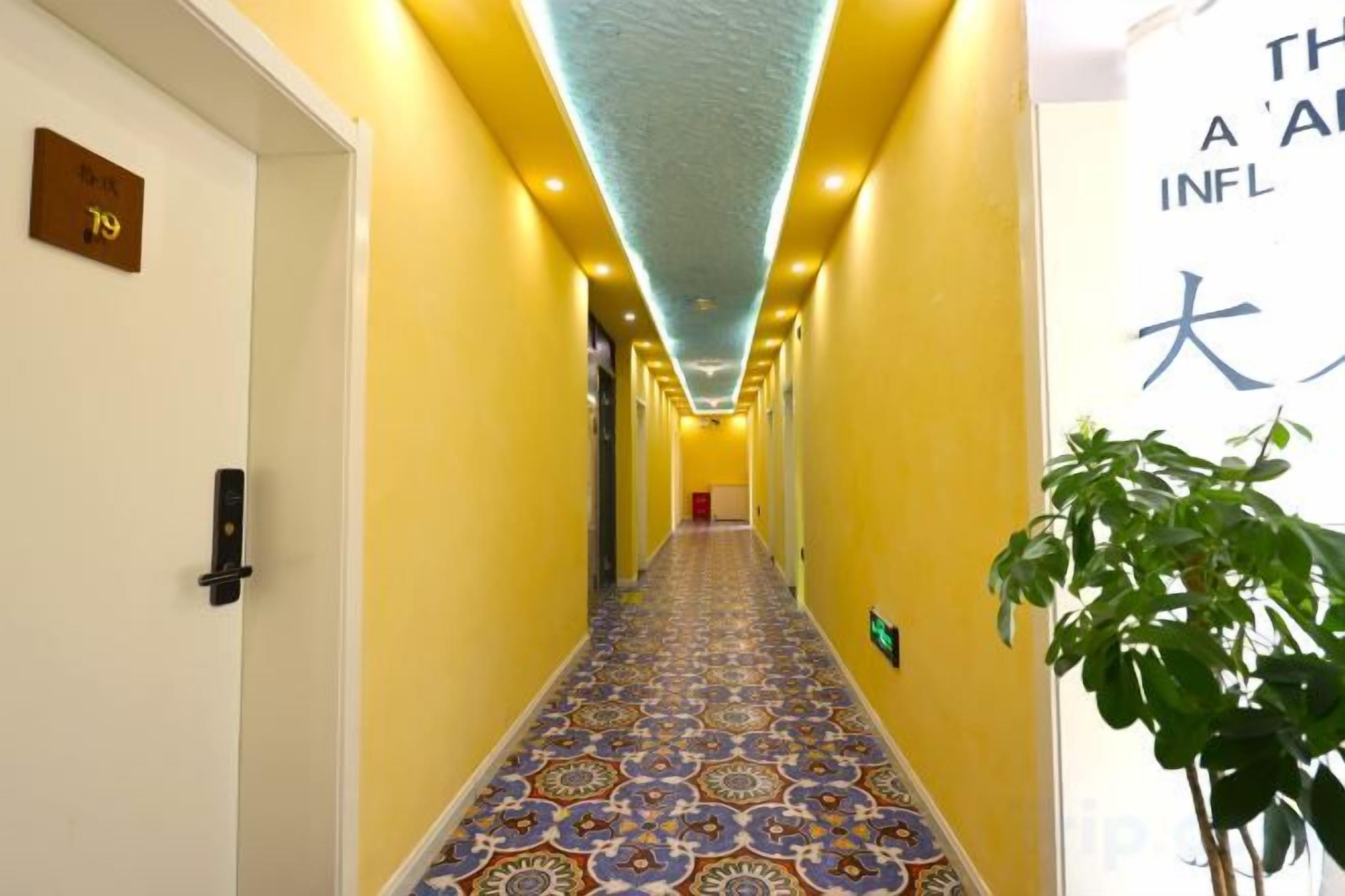 Un couloir d’hôtel avec un tapis à motifs, une plante sur la droite et un panneau avec des caractères japonais.