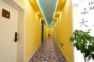 Un pasillo de hotel con alfombra estampada, una planta a la derecha y un cartel con caracteres japoneses.