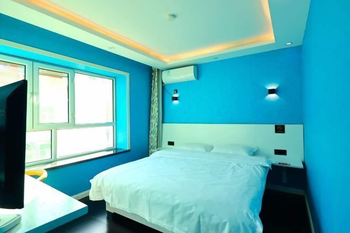 A bedroom with a bed, a window, an air conditioning unit, and a nightstand.