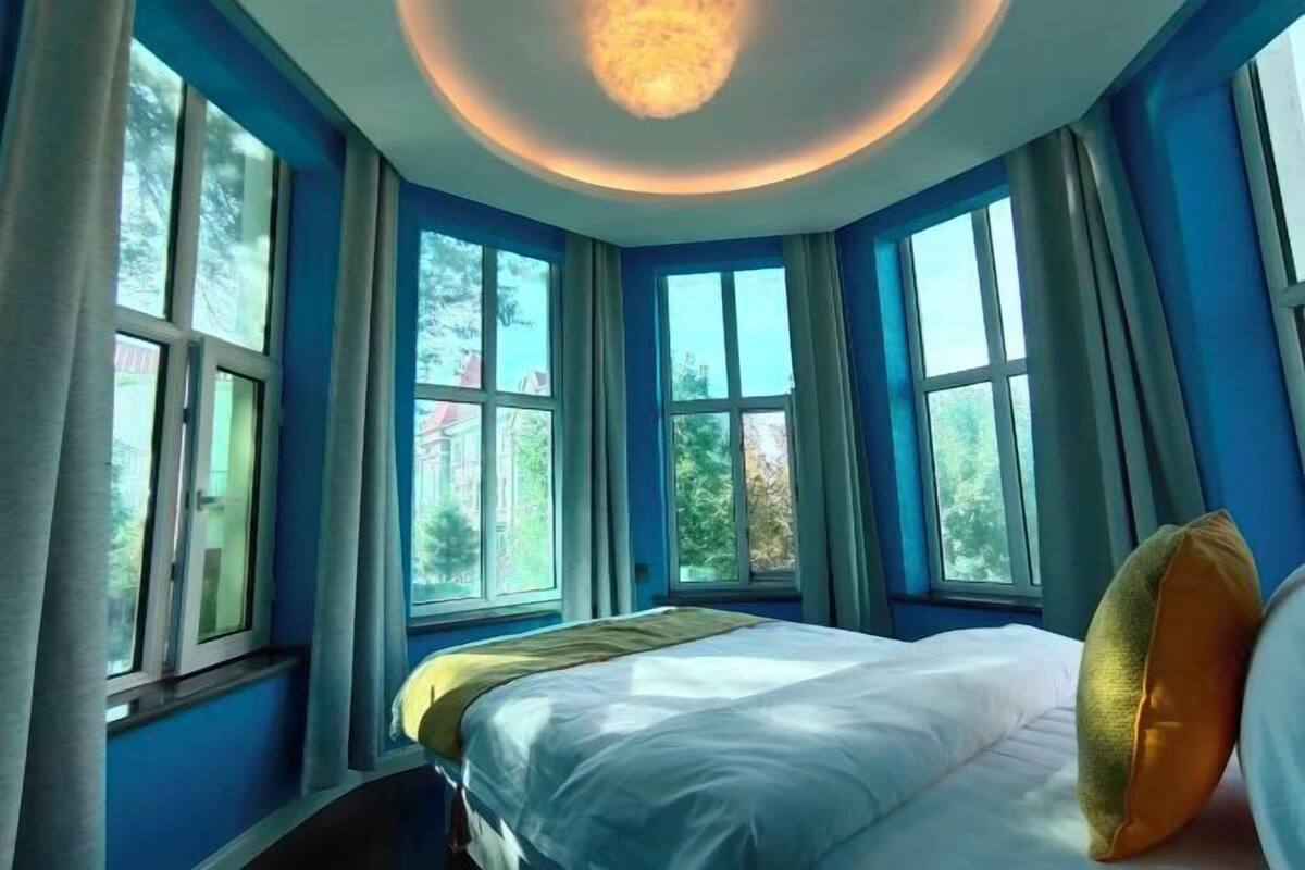 A bedroom with a large bed, multiple windows, and a ceiling light fixture.