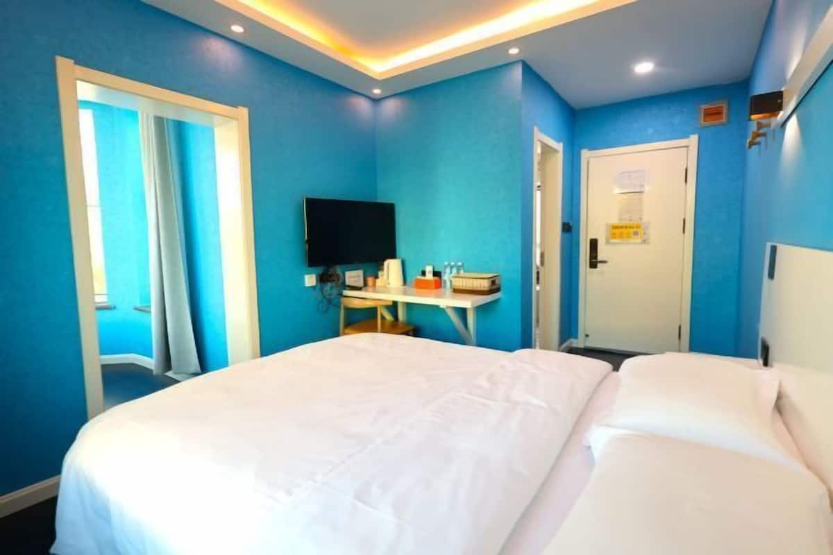 A hotel room with a large bed, a desk with a flat-screen TV, and a door with a sign.