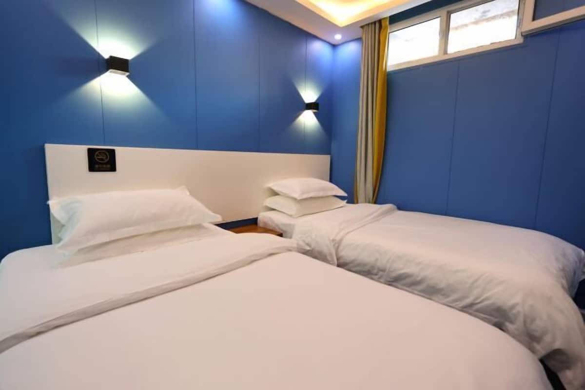 A hotel room with two beds, a headboard with a logo, and wall-mounted lights.