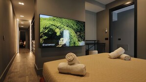 A hotel room with a large flat-screen TV mounted on the wall, a bed with beige bedding and rolled towels, and a wooden floor. - 180M2-Luxurious-Renovated Holiday LOFT, best rental in Olbia (Olbia)