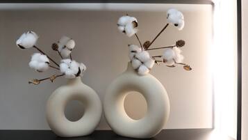 Two white, circular vases with cotton branches and dried leaves on a shelf.