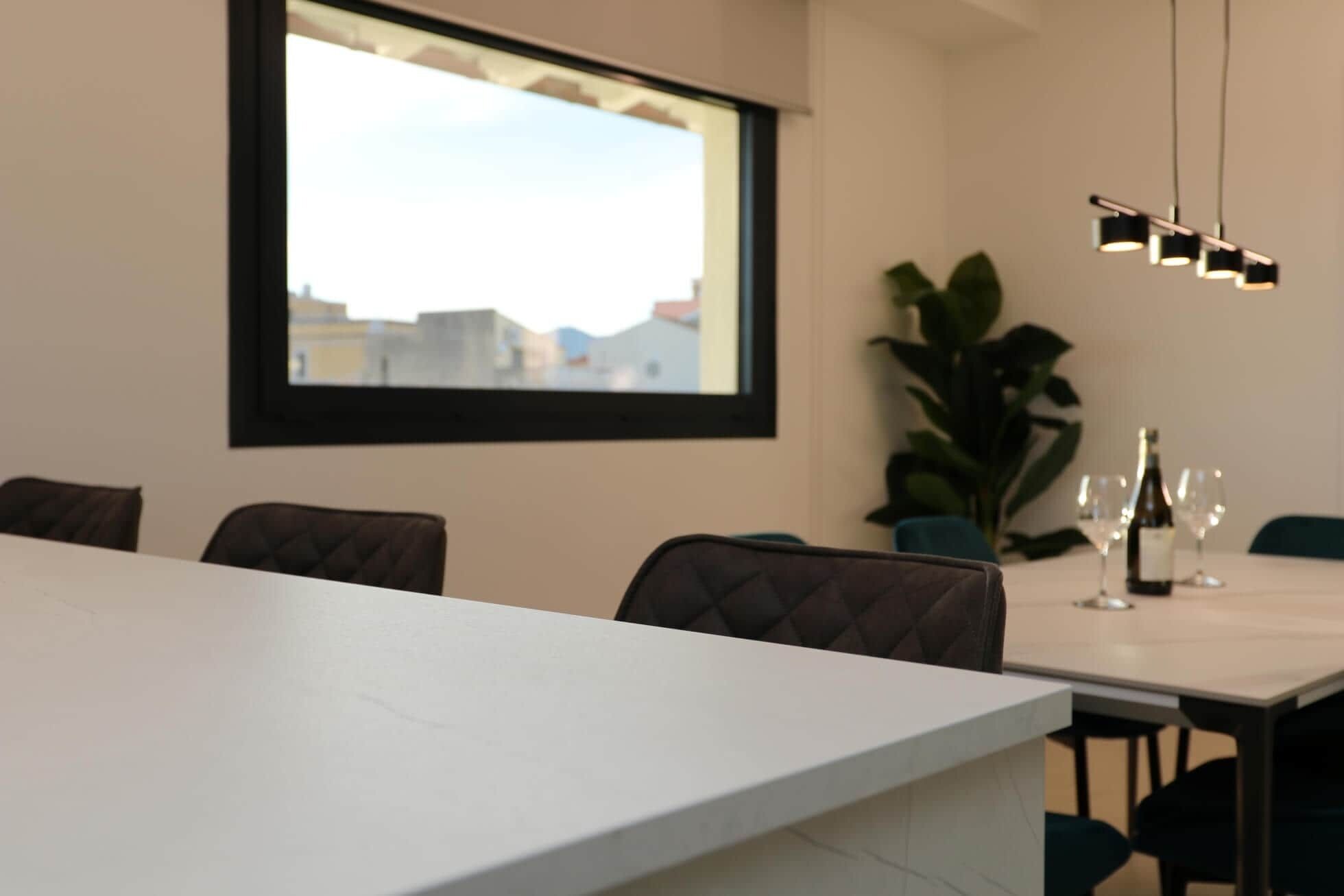 Un espace repas moderne avec une grande fenêtre, une table blanche et un luminaire suspendu.