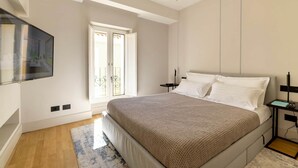 Ein modernes Schlafzimmer mit einem großen Bett, einem an der Wand befestigten Fernseher und einer Glastür zum Balkon.