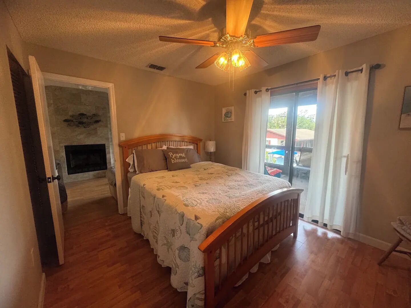 A bedroom with a wooden bed, a ceiling fan, and a view of the outside through a sliding glass door.