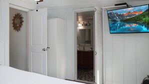 Een slaapkamer met een bed, een aan de muur bevestigde televisie en een deur naar een badkamer.