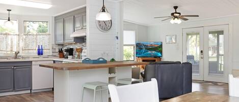 A spacious kitchen with a central island, white bar stools, and a dining table.