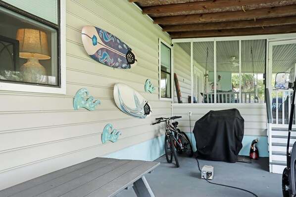 A covered porch with a table, a bicycle, and a surfboard on the wall. - Livin' Like Larry (Port St. Joe)