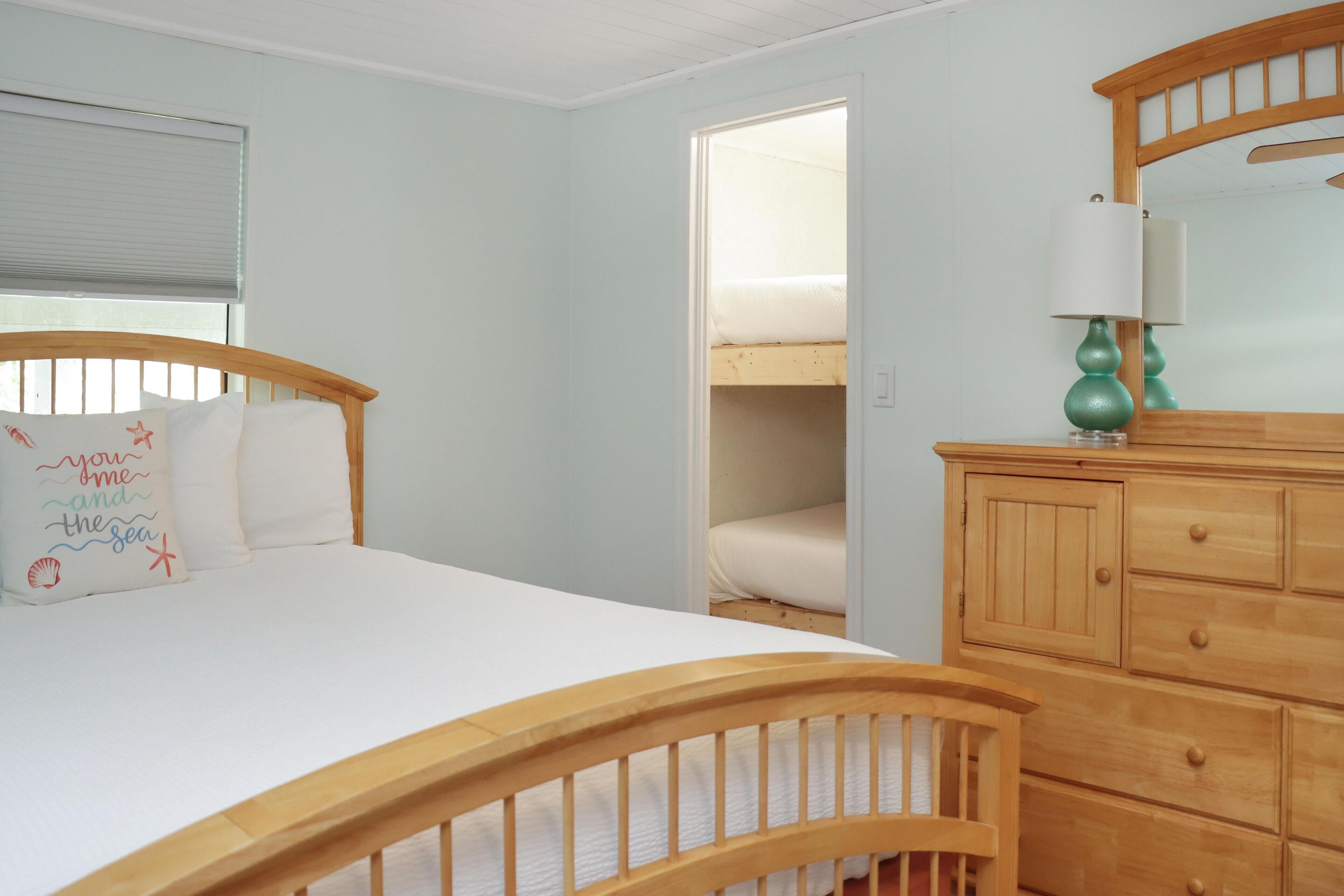 A bedroom with a wooden bed, a dresser, a mirror, and a window with blinds.