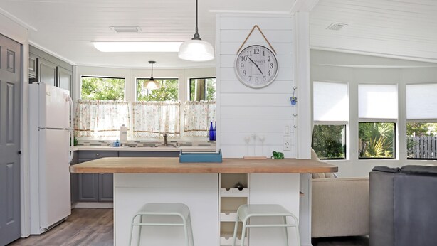 Een moderne keuken met een houten eiland, witte barstoelen en een klok aan de muur.