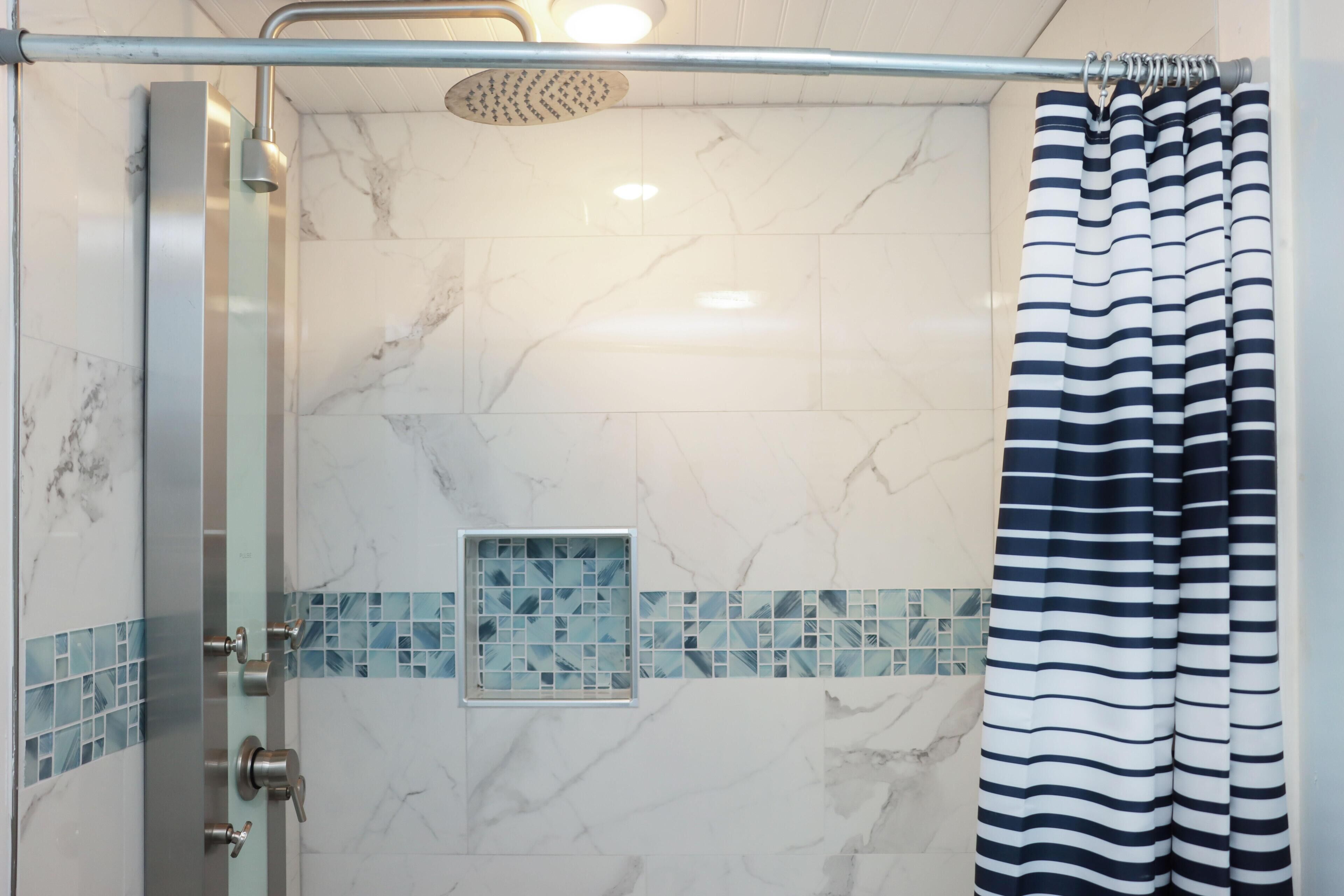 A shower area with a glass door, a rain showerhead, and a striped curtain.
