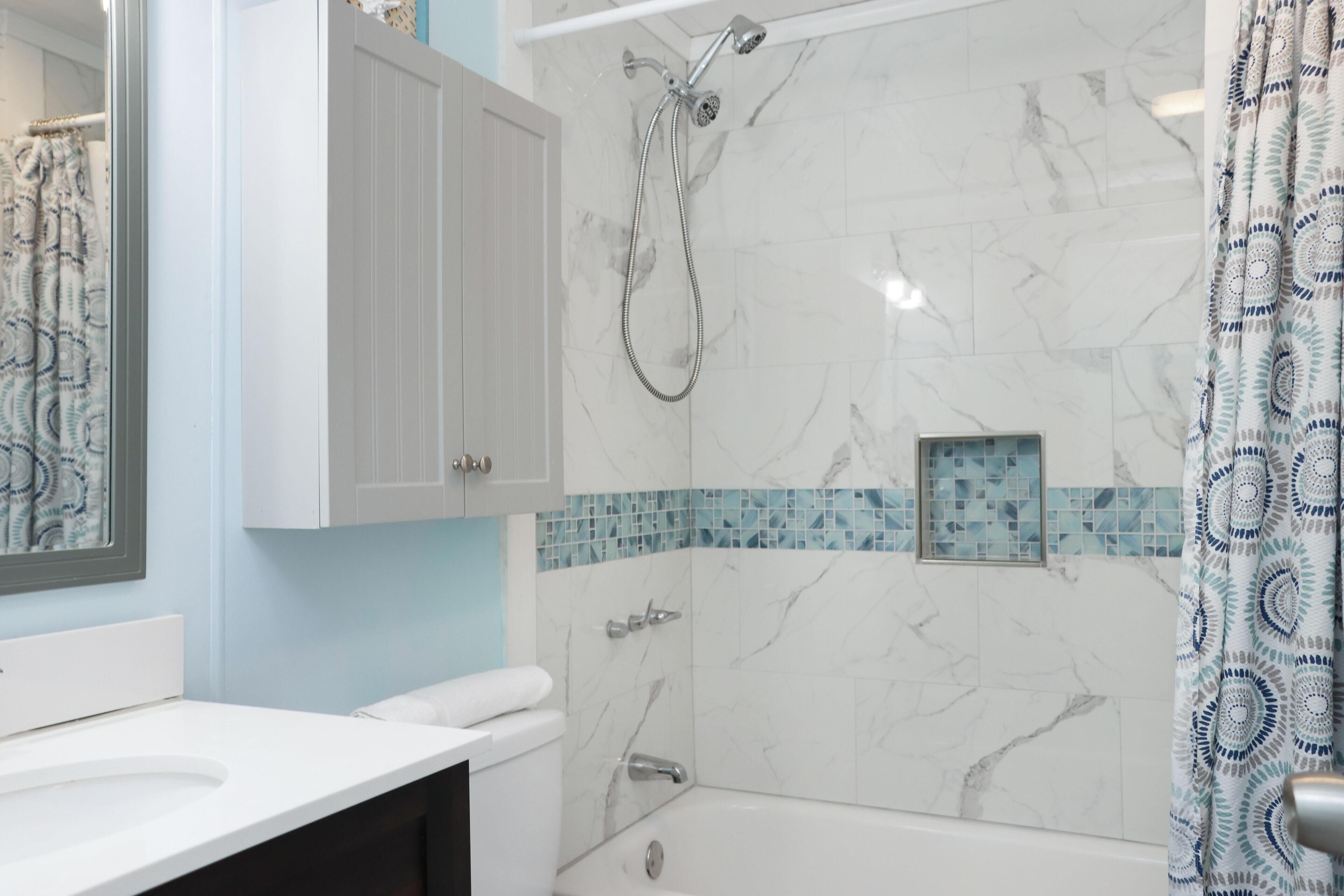 A bathroom with a white vanity, a shower with a handheld showerhead, and a tiled shower wall.