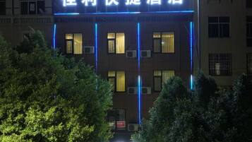 A hotel with illuminated signage in a foreign language, surrounded by trees.