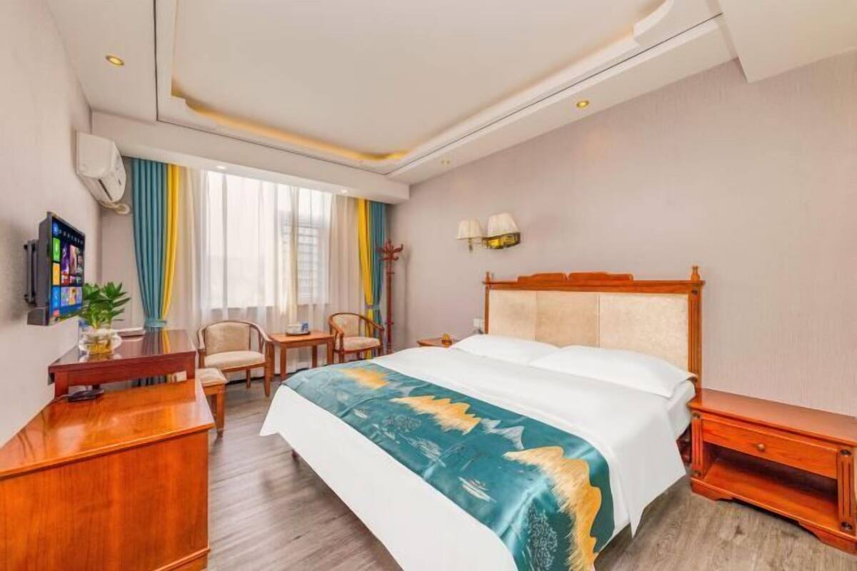 A hotel room with a bed, a desk, a chair, a TV, and a window with curtains.