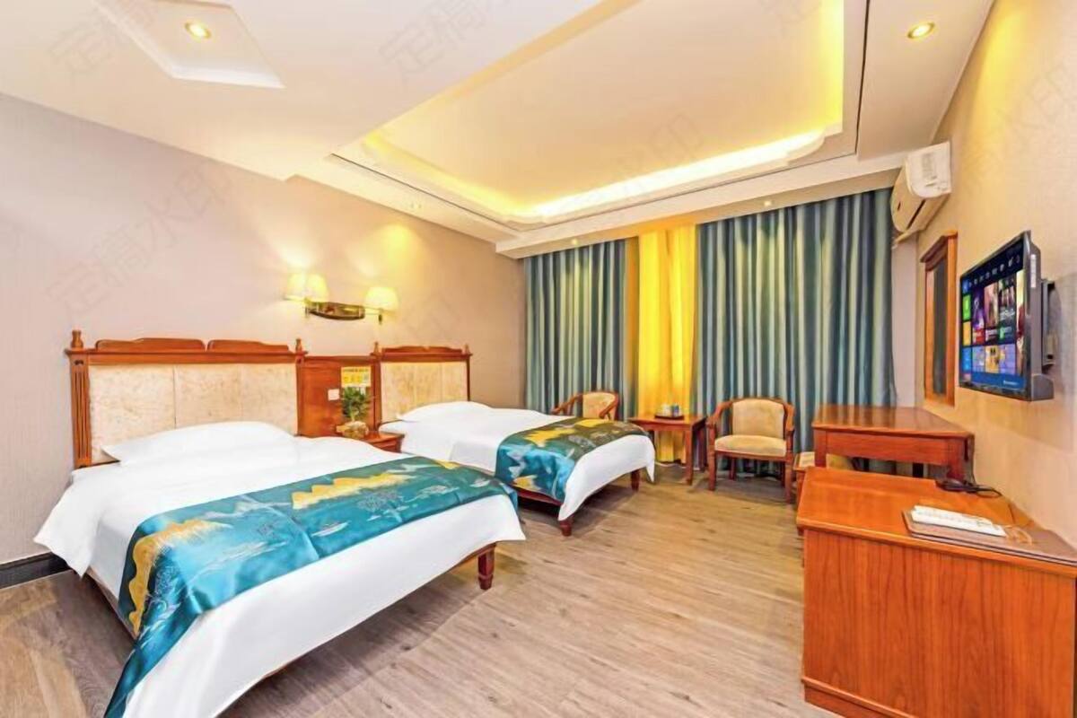 A hotel room with two beds, a desk, a chair, a television, and a curtain.
