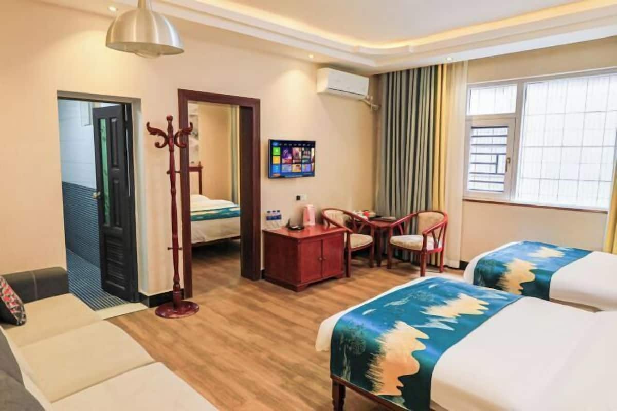 A hotel room with two beds, a desk, a chair, a small table, a TV, and a window with curtains.