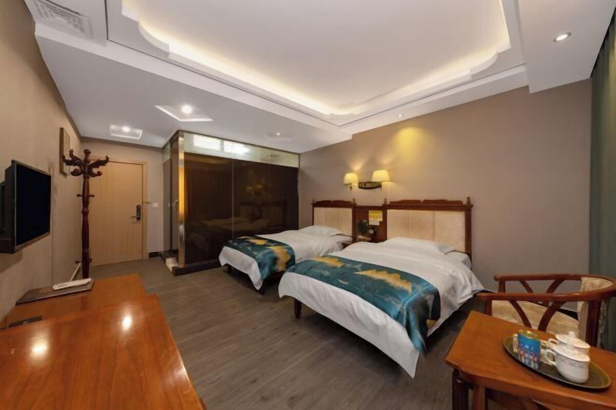 Habitación de hotel con dos camas, un escritorio de madera, una silla, televisión y una puerta corredera que da a un baño.