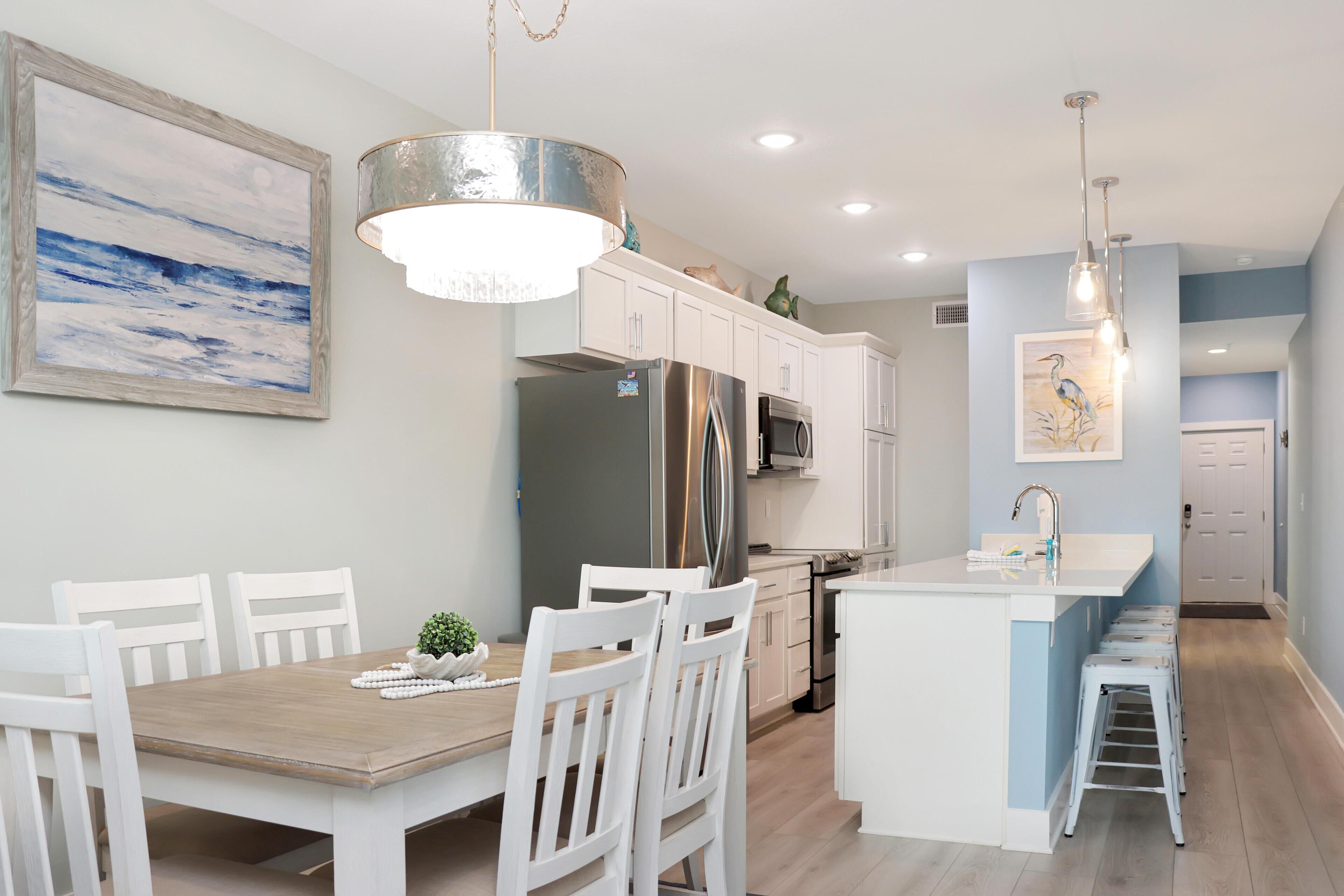 Una cocina moderna con muebles blancos, una isla central y un comedor con sillas blancas.