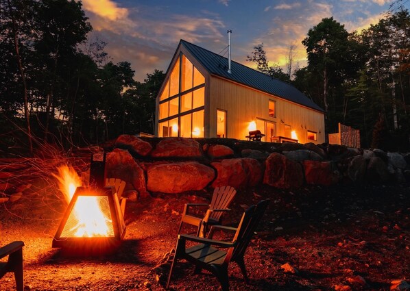 A modern house with a stone wall, a fire pit, and two chairs. - Mont-Tremblant North side | Scandinavian Chalet with Spa (Les Laurentides)