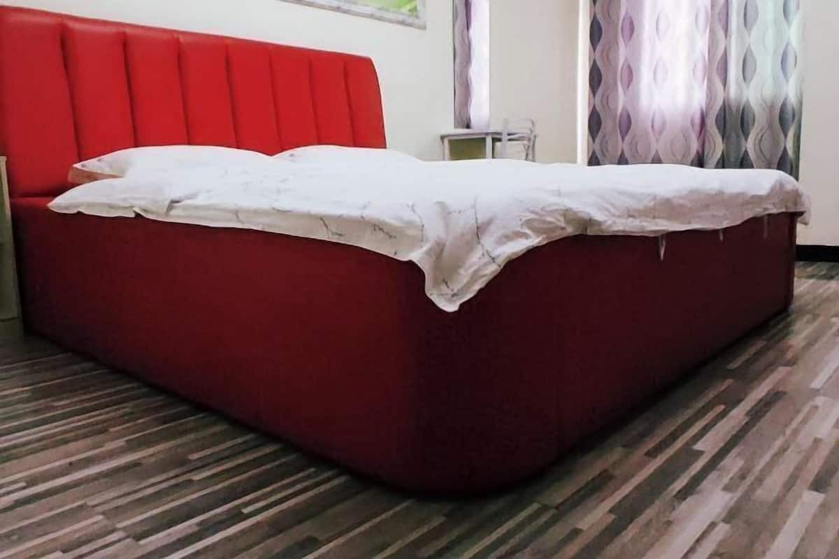 A red bed with white bedding in a room with striped flooring and a window with curtains.