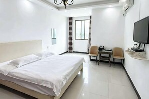 Une chambre d’hôtel avec un lit, un bureau et une chaise, une télévision et une fenêtre avec des rideaux.