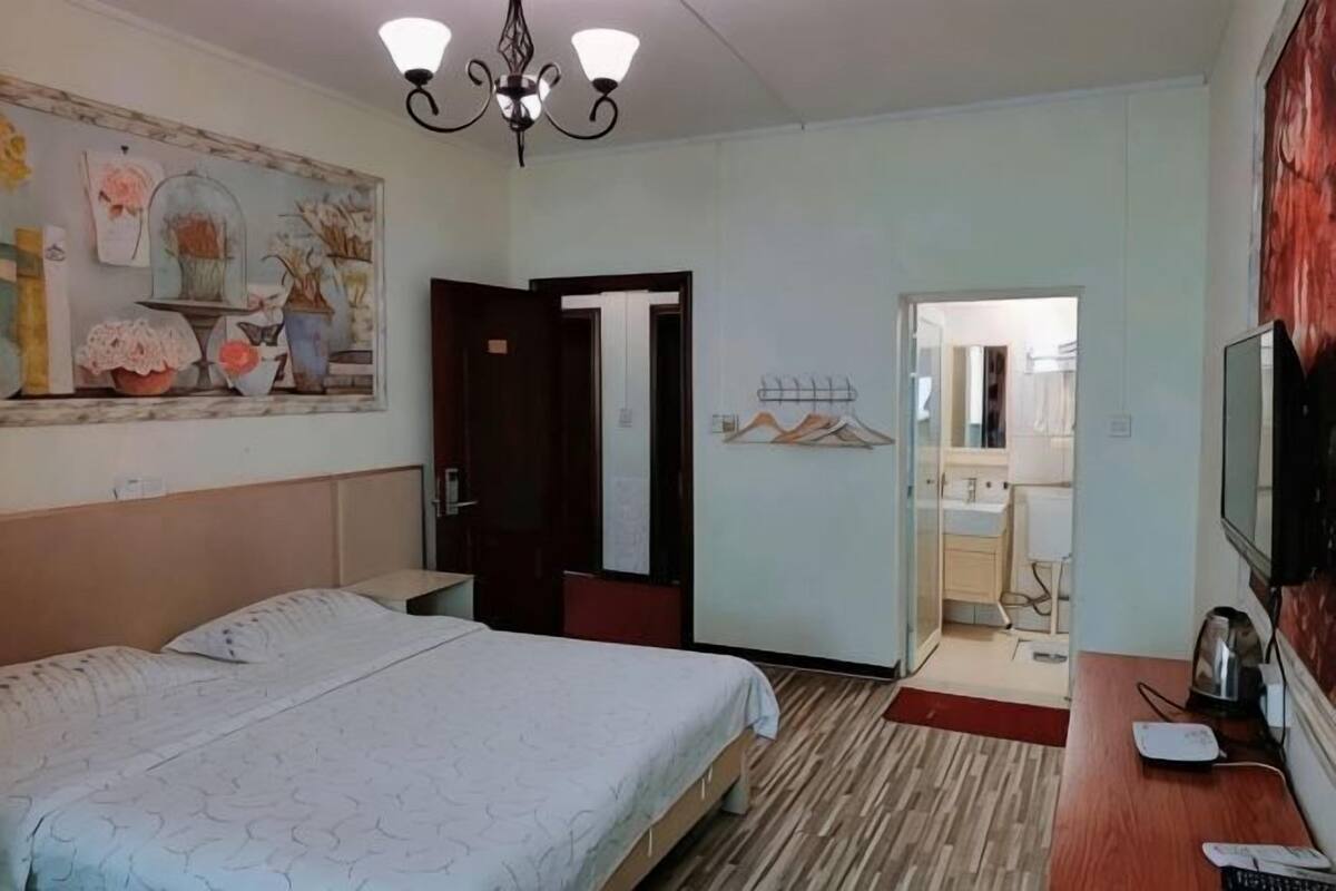 A hotel room with a bed, a desk with a computer, a TV, and a door leading to a bathroom.