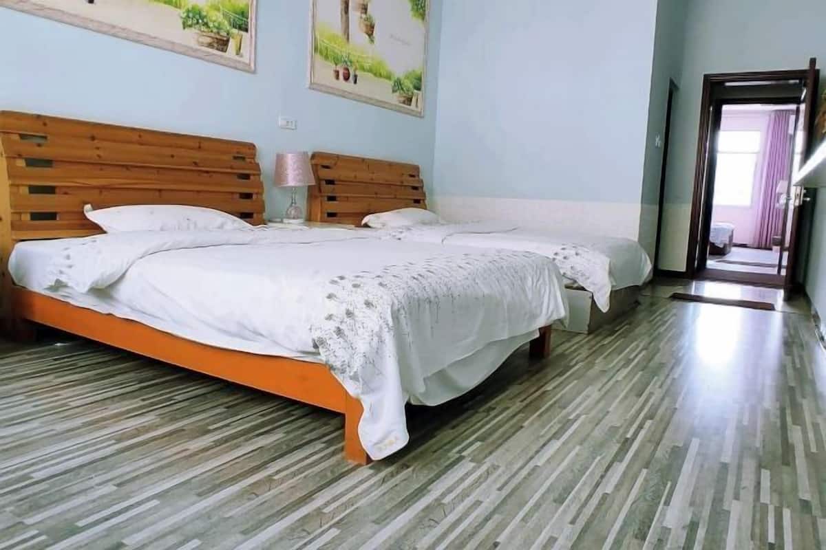 A room with two beds, a wooden headboard, a patterned floor, and a door leading to another room.