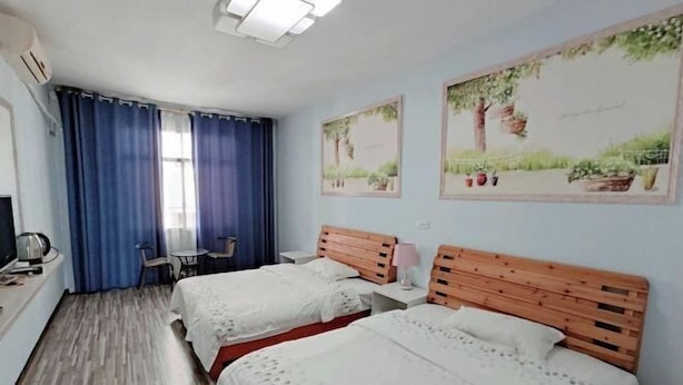 A hotel room with two beds, a desk with a chair, a small table, and a window with blue curtains. - An Inn (Guilin Yiyuan Branch) (Guilin)