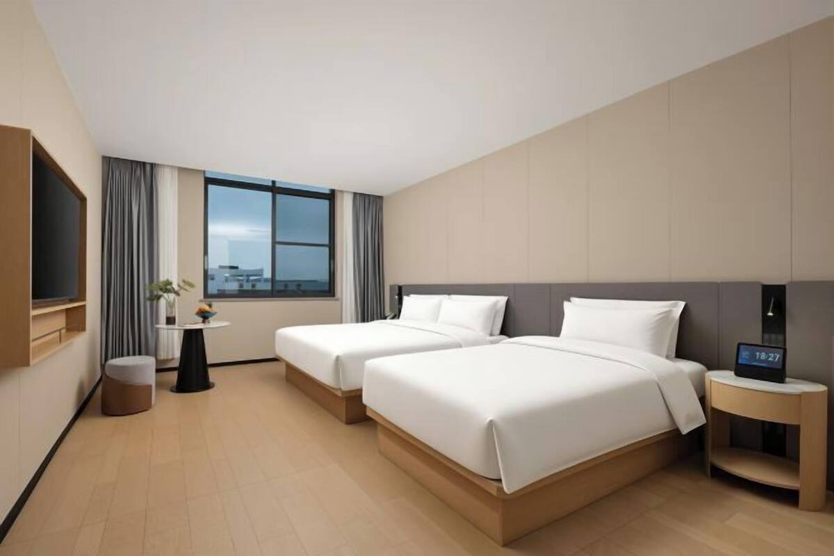 Quarto de hotel com duas camas, televisão, mesa pequena e janela com vista.