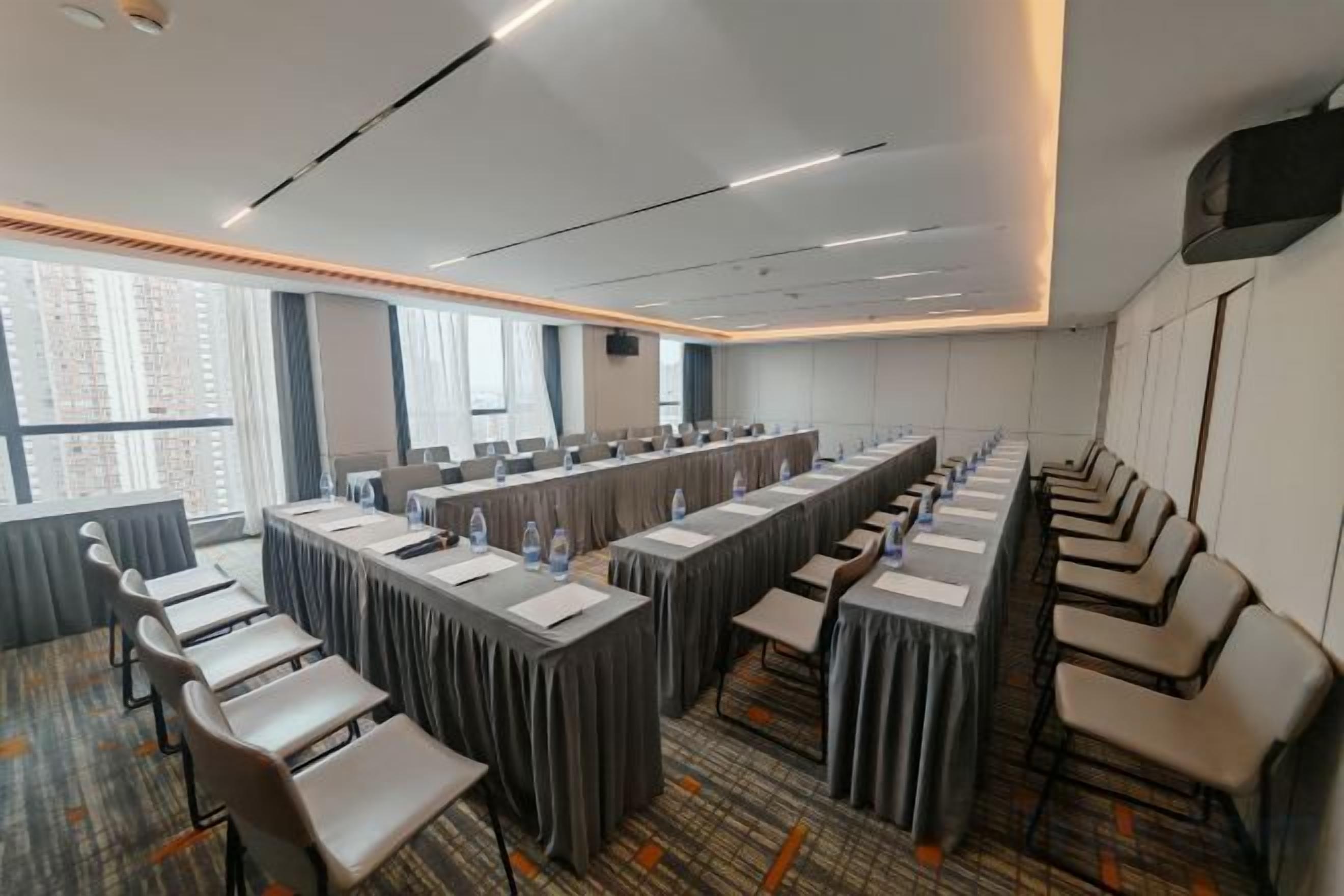 A conference room with long tables, chairs, and a projector screen.