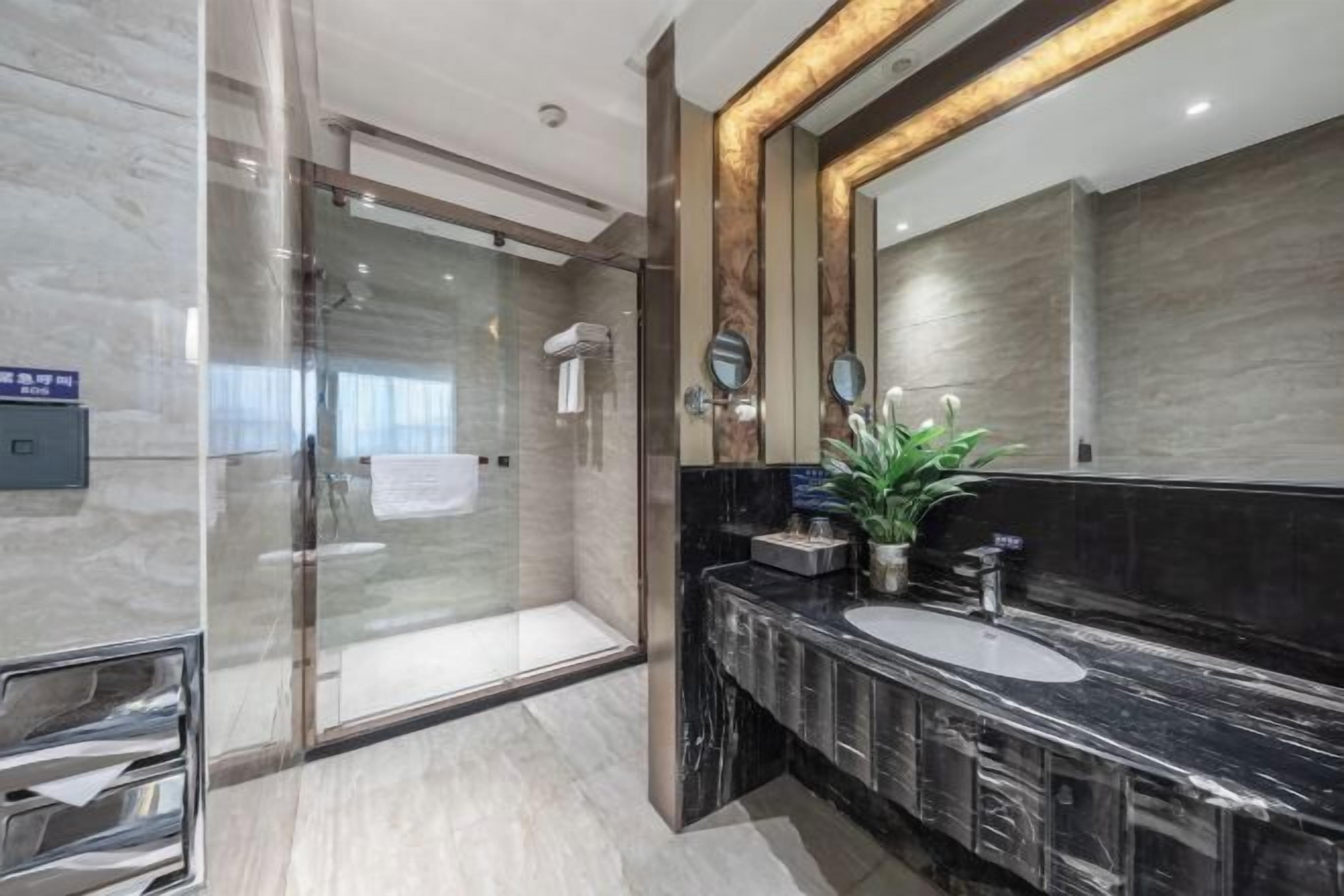 A modern bathroom with a glass shower enclosure, a large mirror, and a marble countertop.
