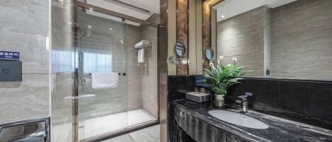 A modern bathroom with a glass shower enclosure, a large mirror, and a marble countertop.