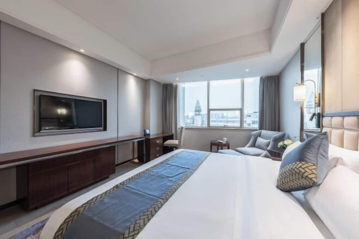 Quarto de hotel com uma cama grande, televisão de tela plana na parede, uma mesinha e uma cadeira.