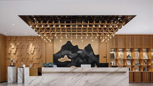 A reception desk with a marble top, a wooden reception desk, a wall with a geometric pattern, and a hanging light fixture. - haofeng S hotel (Chengdu)